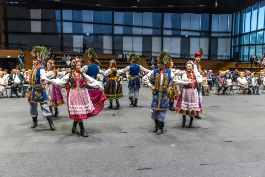 Grupa tancerzy w tradycyjnych strojach ludowych tańczy na scenie.