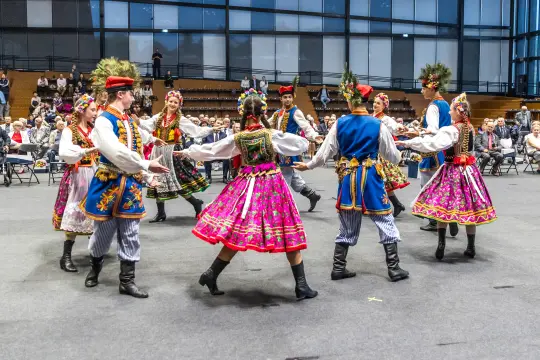 Tradycyjny taniec ludowy w kolorowych strojach, uczestnicy w kręgu.