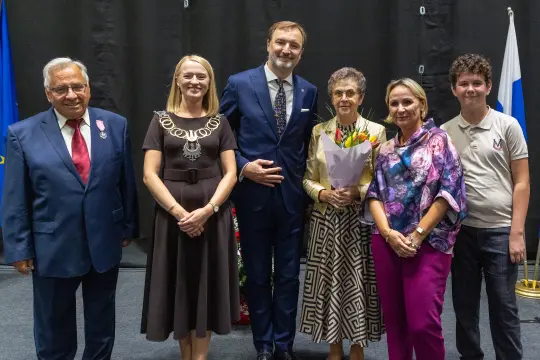 Grupa osób pozujących do zdjęcia, w tym kobieta z bukietem kwiatów.