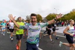 Biegacze uczestniczą w maratonie, jeden z nich uśmiecha się i unosi ręce w geście radości.