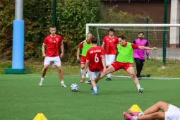 Trening drużyny piłkarskiej na boisku, zawodnicy w czerwonych strojach.