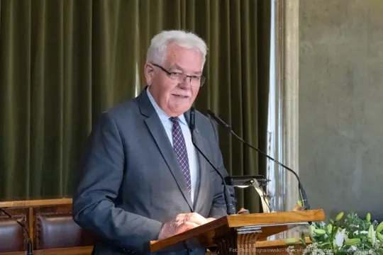 Mężczyzna przemawia z mównicy w sali konferencyjnej.