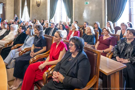 Grupa kobiet siedzących w sali, uczestniczących w wydarzeniu formalnym.