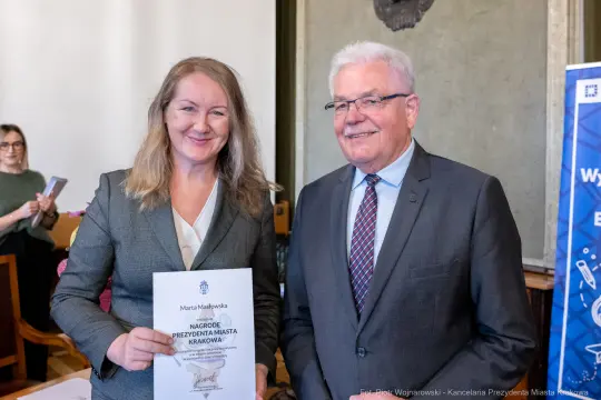 Wręczenie nagrody Prezydenta Miasta Krakowa. Dwie osoby uśmiechnięte, trzymające dokument.