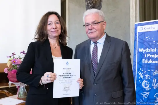 Kobieta i mężczyzna trzymają dyplom nagrody w sali z dekoracjami.