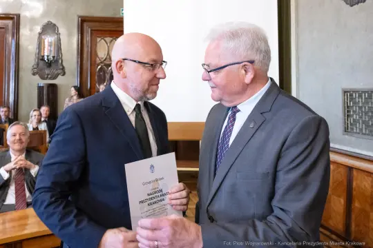 Wręczenie nagrody Prezydenta Miasta Krakowa. Dwie osoby w formalnych strojach, dokument w rękach jednego z nich.