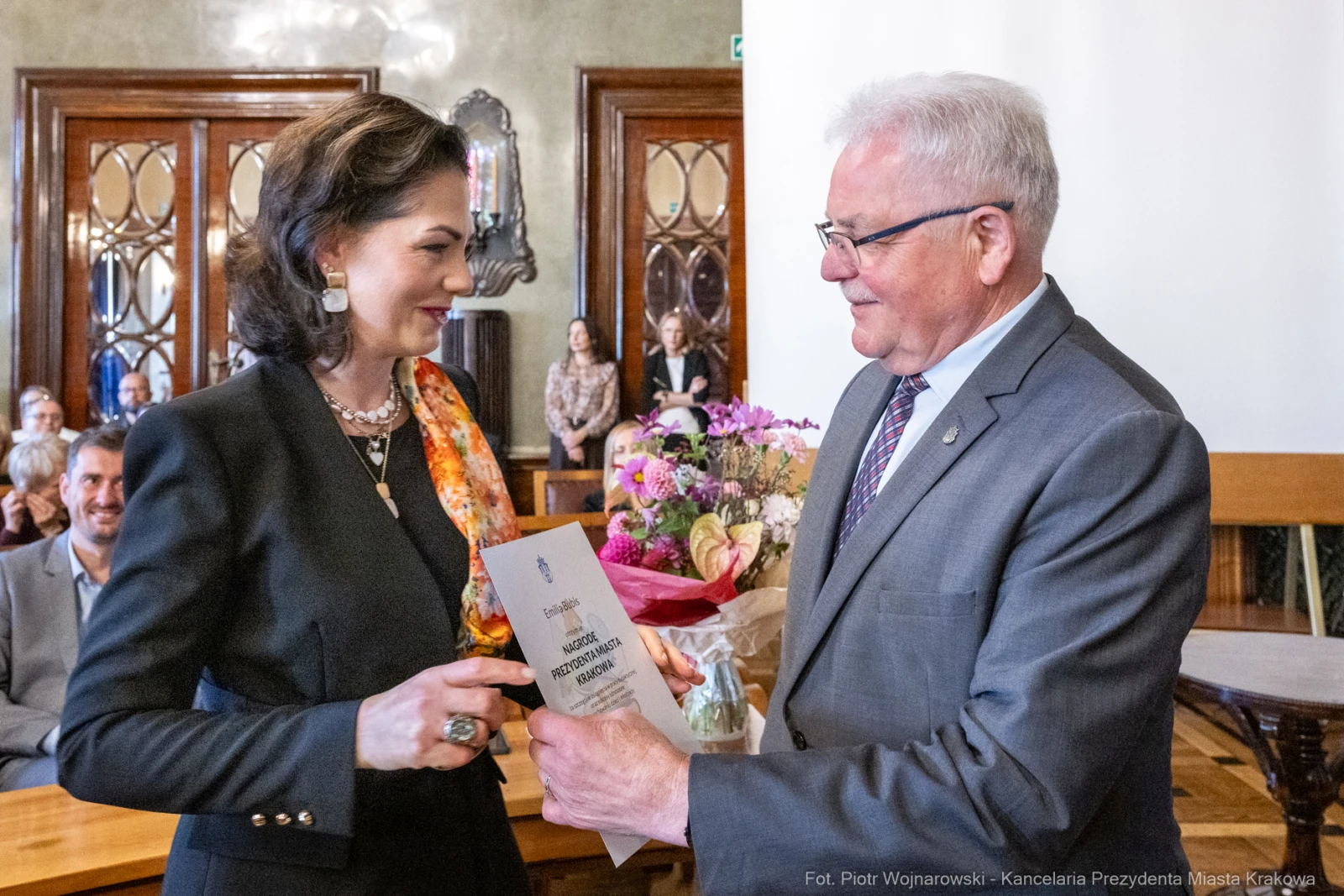 Wręczenie nagrody z bukietem kwiatów w tle, uśmiechnięte osoby w eleganckich strojach.  Autor: Piotr Wojnarowski