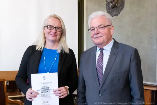 Kobieta z dyplomem i mężczyzna w garniturze, oboje uśmiechnięci.