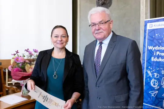 Wręczenie dyplomu przez kobietę i mężczyznę w formalnym otoczeniu.