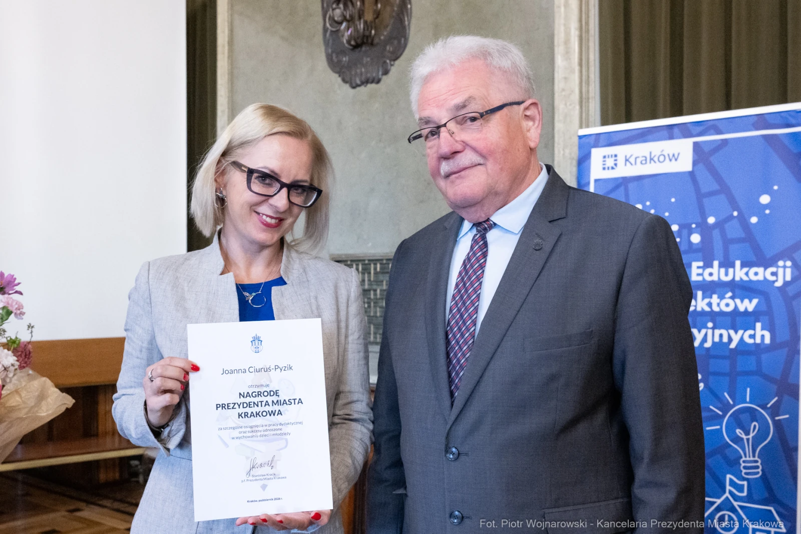 Kobieta i mężczyzna trzymają dyplom nagrody w sali z dekoracjami.  Autor: Piotr Wojnarowski