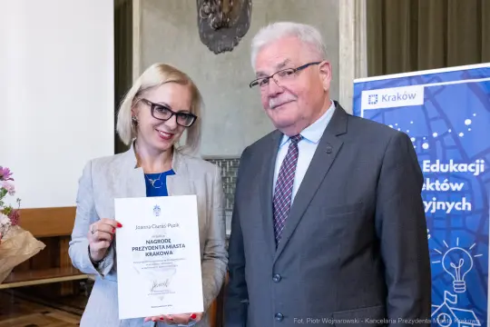 Kobieta i mężczyzna trzymają dyplom nagrody w sali z dekoracjami.