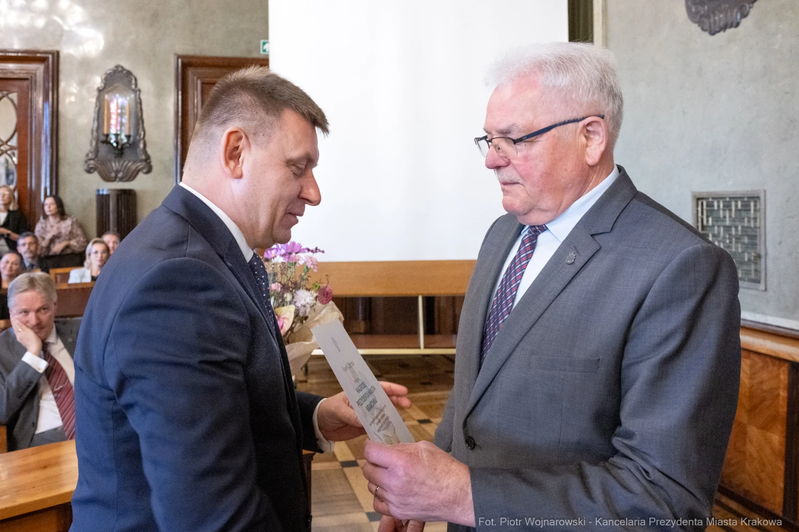 Wręczenie nagrody w sali obrad, dwóch mężczyzn w formalnych strojach, kwiaty na stole.  Autor: Piotr Wojnarowski