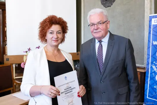 Kobieta i mężczyzna trzymają dyplom w sali z dekoracjami.