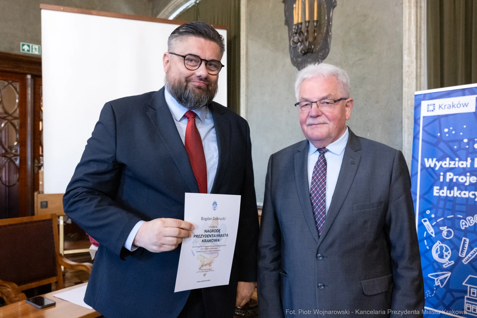 Dwaj mężczyźni trzymają dokument, uśmiechając się do kamery w sali konferencyjnej.  Autor: Piotr Wojnarowski