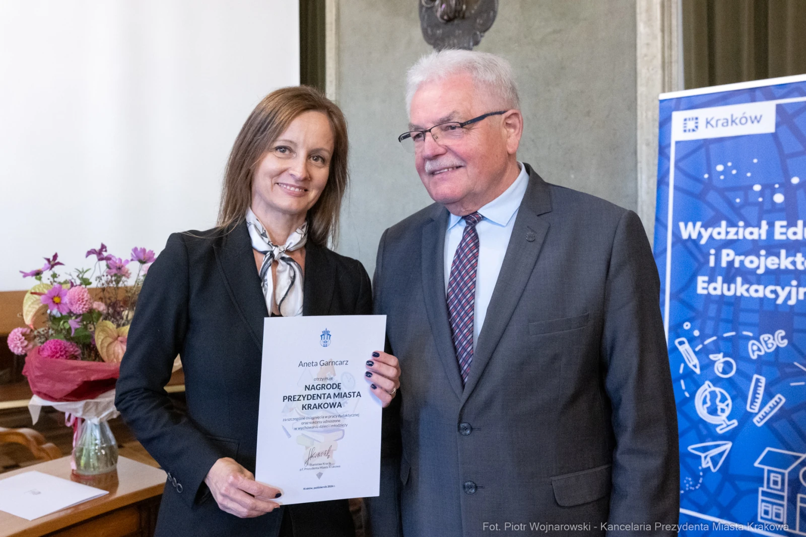 Kobieta odbierająca nagrodę od mężczyzny w formalnym otoczeniu.  Autor: Piotr Wojnarowski