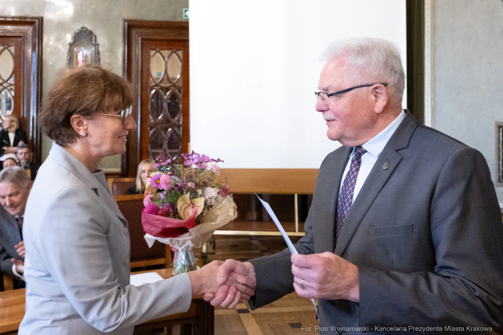 Uścisk dłoni między dwiema osobami, jedna z bukietem kwiatów.  Autor: Piotr Wojnarowski