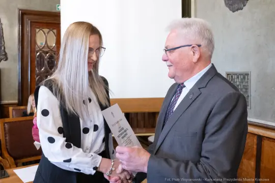 Wręczenie dyplomu przez mężczyznę kobiecie w sali konferencyjnej.