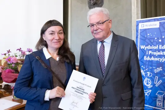Kobieta i mężczyzna trzymają dyplom w sali z dekoracjami.