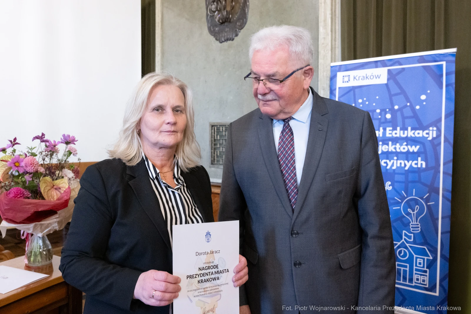 Wręczenie nagrody przez przedstawiciela miasta Krakowa. Kobieta z dyplomem i bukietem kwiatów.  Autor: Piotr Wojnarowski