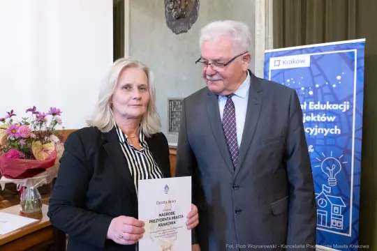 Wręczenie nagrody przez przedstawiciela miasta Krakowa. Kobieta z dyplomem i bukietem kwiatów.