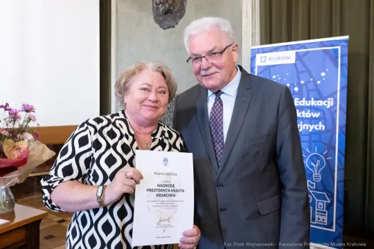 Kobieta odbierająca nagrodę od mężczyzny w garniturze, trzymająca dyplom.