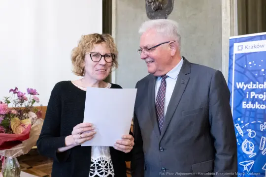 Uśmiechnięte osoby trzymające dokument w otoczeniu kwiatów.