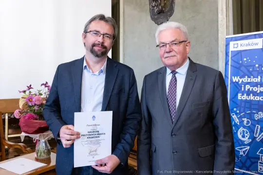 Dwaj mężczyźni trzymają dyplom w sali wykładowej.