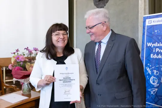 Kobieta trzymająca dyplom, obok niej mężczyzna, oboje uśmiechnięci.