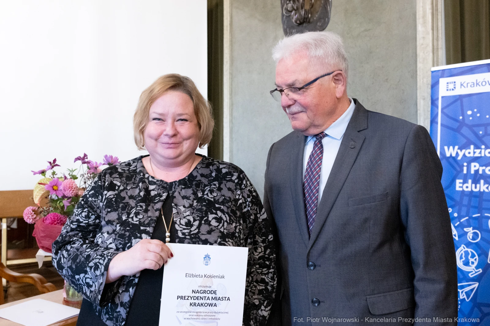 Kobieta z dyplomem nagrody Prezydenta Miasta Krakowa, obok mężczyzna w garniturze.  Autor: Piotr Wojnarowski