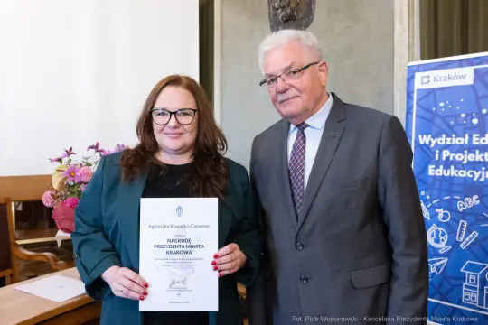 Kobieta i mężczyzna trzymają dyplom w sali z elementami dekoracyjnymi.
