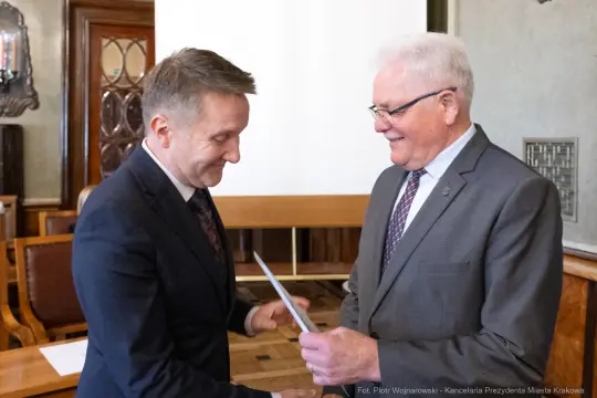 Dwaj mężczyźni uśmiechają się i wymieniają dokumenty w eleganckim wnętrzu.