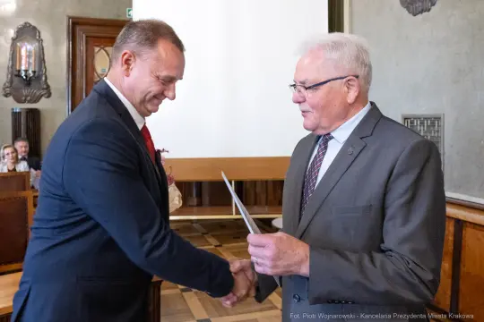 Mężczyźni uścisnęli sobie dłonie podczas wręczenia dyplomu w sali konferencyjnej.