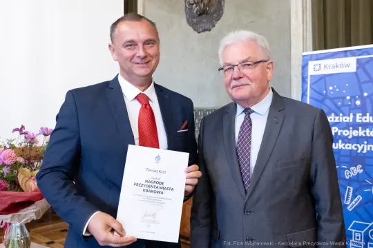 Mężczyźni trzymający dyplom nagrody w sali konferencyjnej.