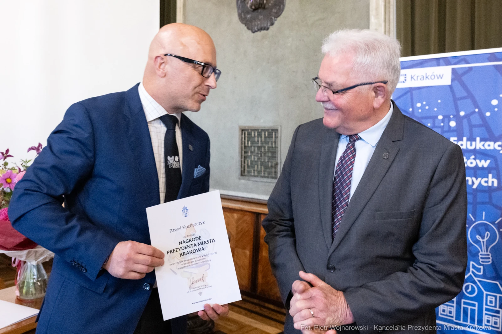 Mężczyźni wręczają sobie dyplom w sali z dekoracjami.  Autor: Piotr Wojnarowski