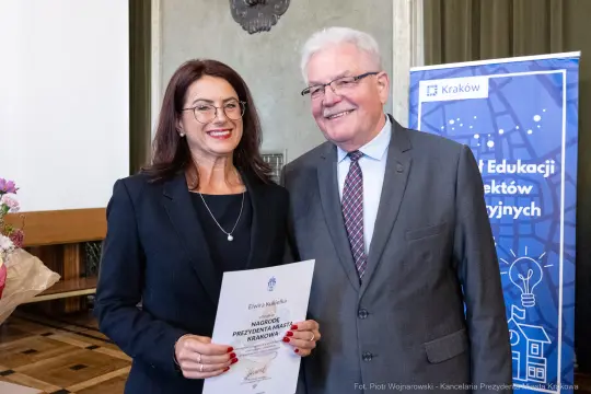 Wręczenie nagrody przez uśmiechnięte osoby, jedna z nich trzyma dyplom.