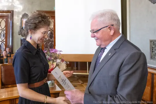 Wręczenie dyplomu z kwiatami w eleganckiej sali.