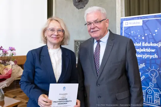Kobieta i mężczyzna trzymają dyplom nagrody w sali z dekoracjami.