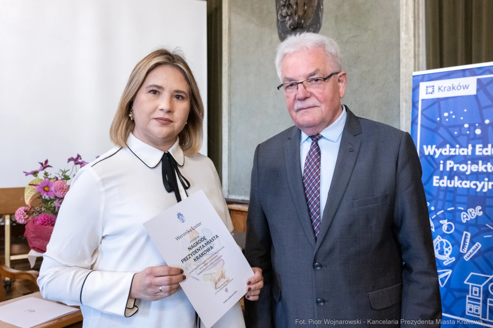 Wręczenie dyplomu przez mężczyznę kobiecie w sali z dekoracjami.  Autor: Piotr Wojnarowski