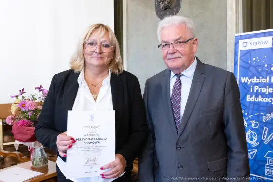 Kobieta i mężczyzna trzymają dyplom w sali urzędowej.