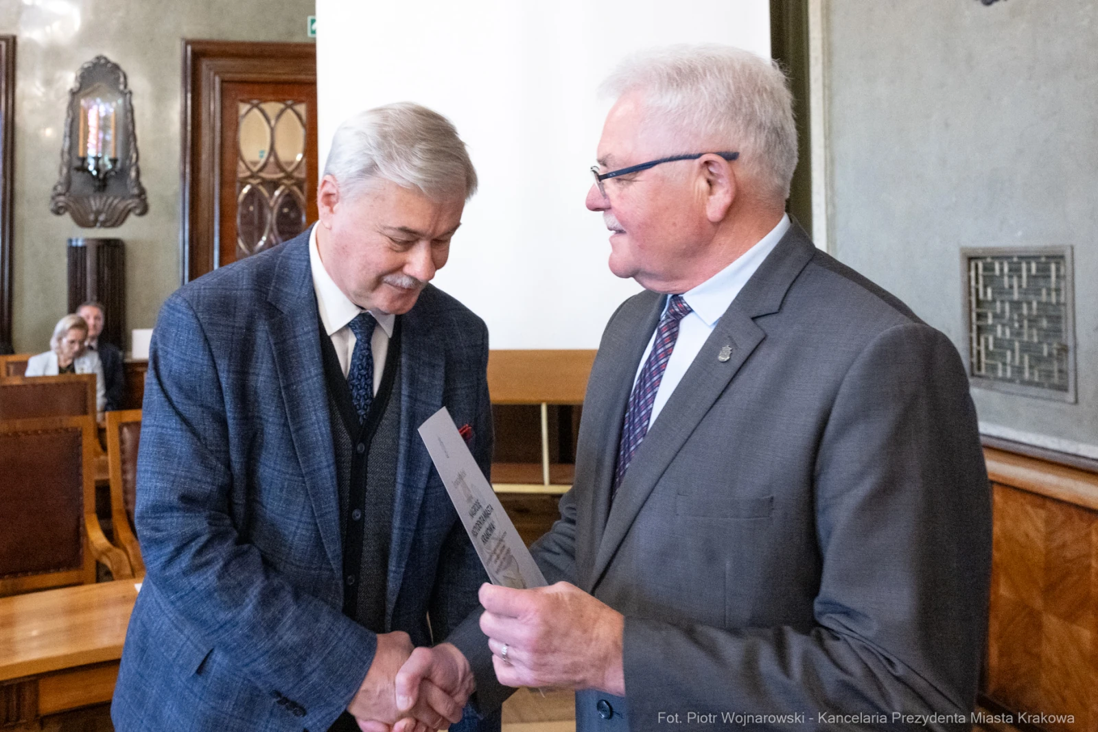 Dwaj mężczyźni wymieniają się dokumentem w eleganckim wnętrzu.  Autor: Piotr Wojnarowski