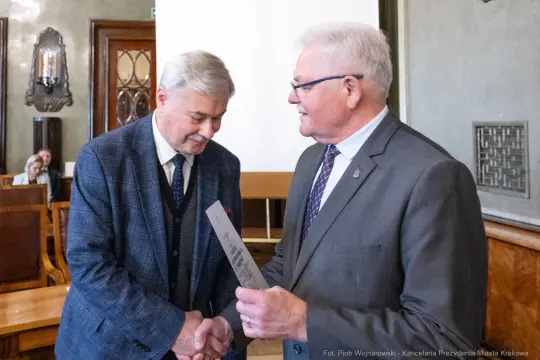 Dwaj mężczyźni wymieniają się dokumentem w eleganckim wnętrzu.