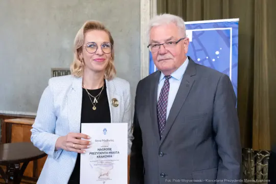 Kobieta i mężczyzna trzymają dyplom nagrody prezydenta miasta Krakowa.