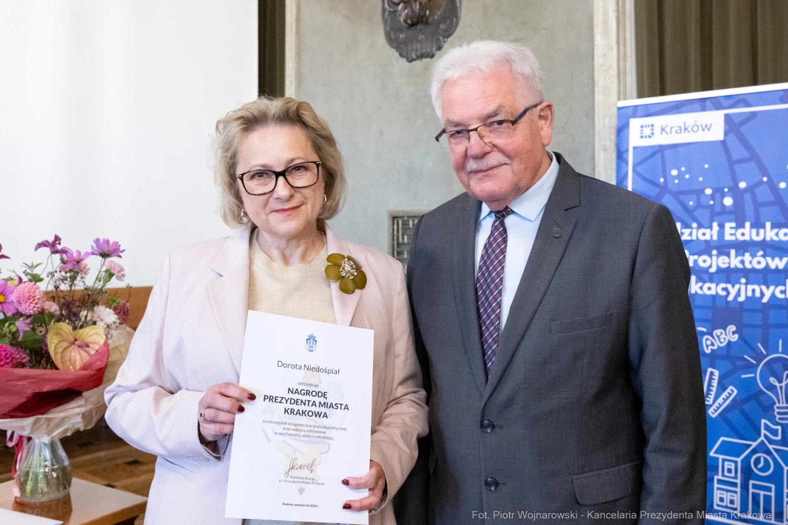 Kobieta i mężczyzna trzymają dyplom nagrody w sali z kwiatami w tle.  Autor: Piotr Wojnarowski