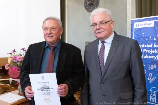 Dwaj mężczyźni trzymają dyplom w sali z dekoracjami.