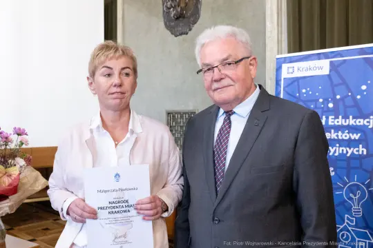 Kobieta z dyplomem i mężczyzna w garniturze, oboje uśmiechnięci.