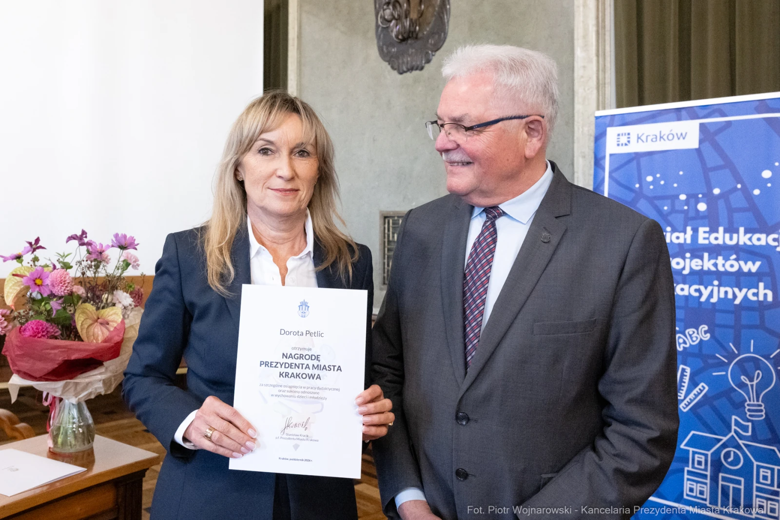 Dorota Pelc odbiera nagrodę od przedstawiciela miasta Krakowa. W tle kwiaty i dekoracje sali.  Autor: Piotr Wojnarowski