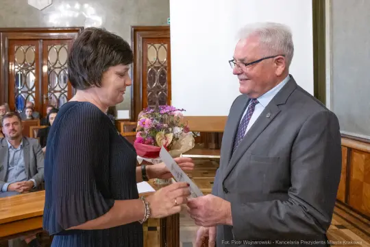 Wręczenie nagrody z bukietem kwiatów w sali urzędowej.
