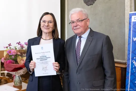 Kobieta z dyplomem i mężczyzna w garniturze, oboje uśmiechnięci.
