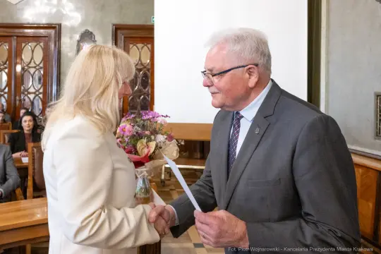 Wręczenie nagrody z okazji wyróżnienia, uściski dłoni, bukiet kwiatów.