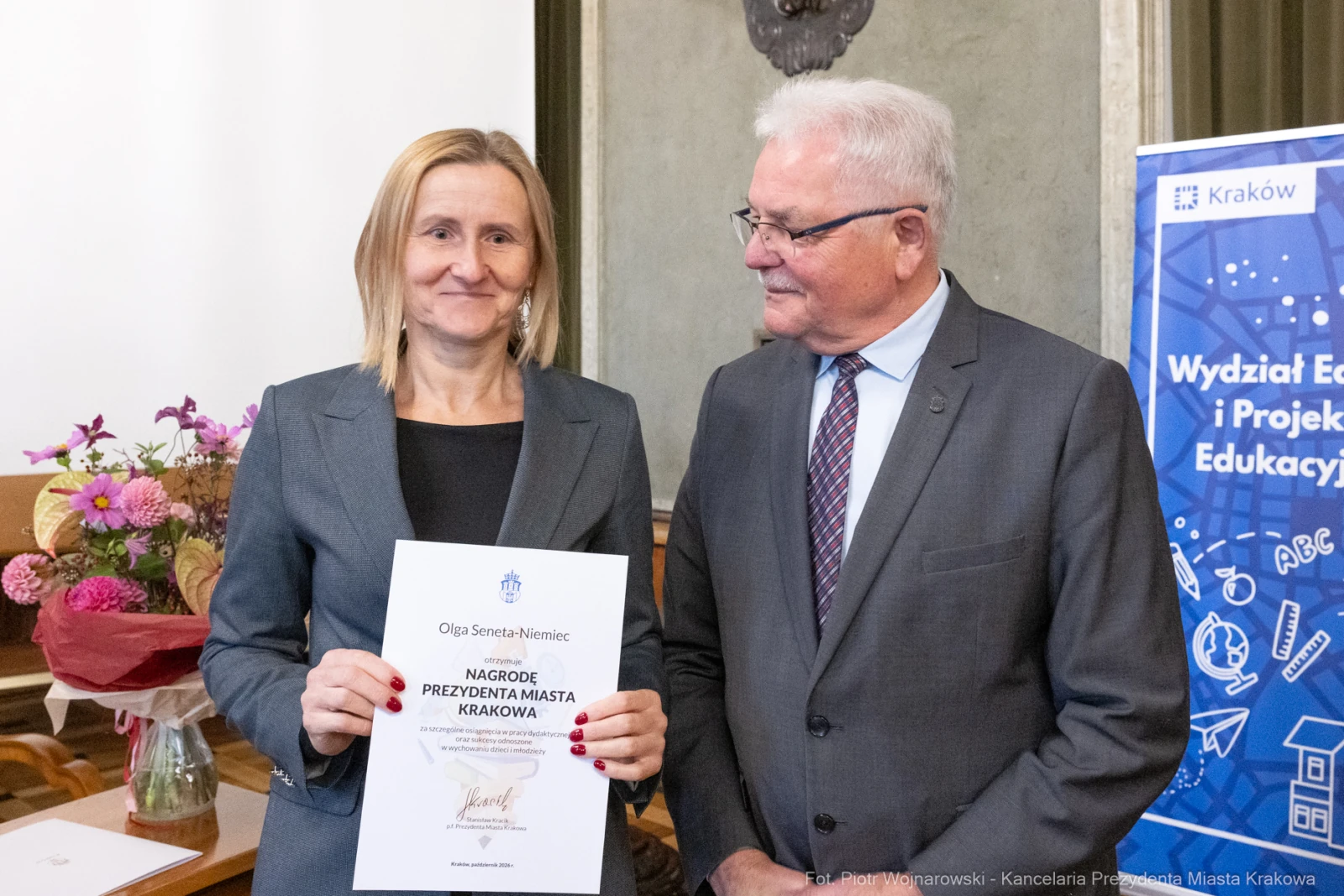 Kobieta z dyplomem nagrody, mężczyzna obok, kwiaty w tle.  Autor: Piotr Wojnarowski